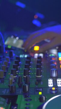 Vertical footage of a DJ mixing on a set in the lights of a dance club