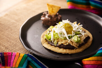 Sopes de Pollo. Traditional homemade Mexican appetizer prepared with fried corn dough covered with refried beans, green or red sauce, lettuce, cheese, onion and shredded chicken