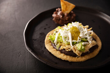 Sopes de Pollo. Traditional homemade Mexican appetizer prepared with fried corn dough covered with refried beans, green or red sauce, lettuce, cheese, onion and shredded chicken