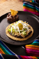 Sopes de Pollo. Traditional homemade Mexican appetizer prepared with fried corn dough covered with refried beans, green or red sauce, lettuce, cheese, onion and shredded chicken