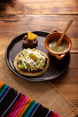 Sopes de Pollo. Traditional homemade Mexican appetizer prepared with fried corn dough covered with refried beans, green or red sauce, lettuce, cheese, onion and shredded chicken