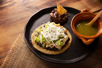 Sopes de Pollo. Traditional homemade Mexican appetizer prepared with fried corn dough covered with refried beans, green or red sauce, lettuce, cheese, onion and shredded chicken