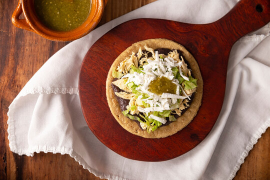 Sopes de Pollo. Traditional homemade Mexican appetizer prepared with fried corn dough covered with refried beans, green or red sauce, lettuce, cheese, onion and shredded chicken