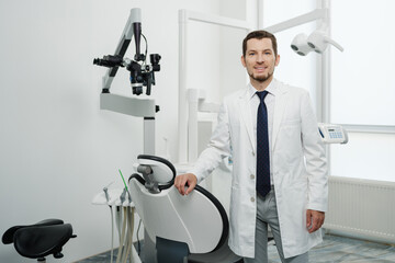Naklejka na ściany i meble Portrait of happy male dentist wearing lab coat in white dental clinic