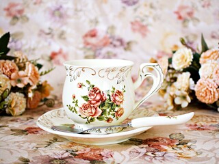 Antique cup of tea with saucer ,yellow orange rose flowers background ,porcelain vintage style ,old English coffee cup still life for wallpaper ,romance roses backgrounds 
