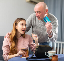 Portrait of a happy couple in which a man gives a credit card to a joyful wife at home