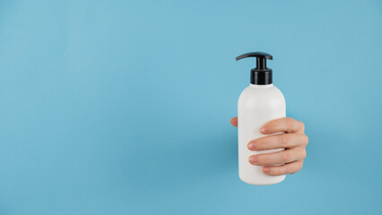 A woman's hand sticks out of a hole in a blue paper background and holds a skin lotion pump.