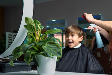 Enthusiastic boy rejoices on an armchair in a hairdressing salon while cutting his hair