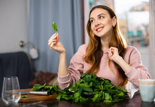 Young European woman, sitting at a table in a room sorts fresh spinach