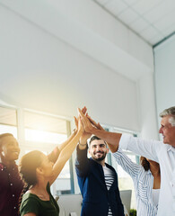 Group of business people doing high five together while standing inside an office with sun flare...