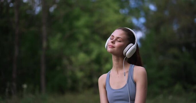 A woman sits on the grass in nature and listens to meditative music on her headphones while sporting her uniform. The concept of self-care and inner psychological state