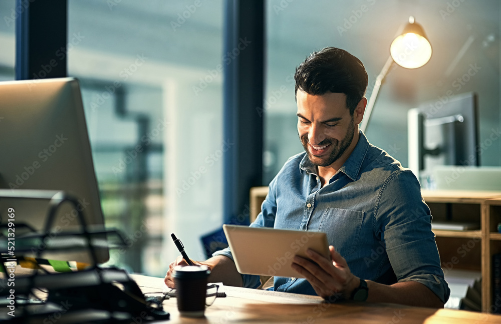 Poster Using his time wisely with smart technology. Shot of a young businessman using a digital tablet during a late night at work.