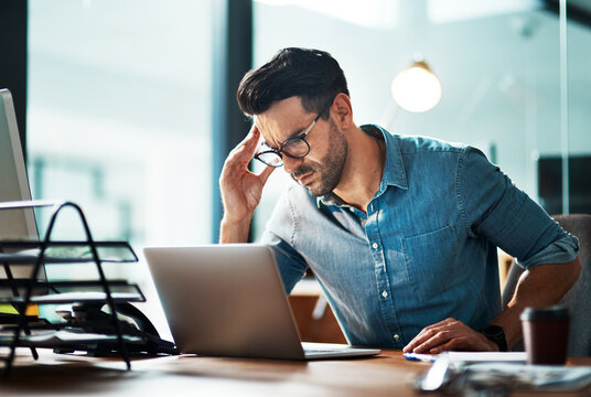 Businessman suffering from a headache or migraine due to stress caused by work deadlines. Professional holding head in pain feeling anxious, overwhelmed and stressed while busy on his computer desk