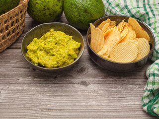 Top view of fresh guacamole in a dish and potato chips on a plate over a wooden table