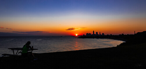 Fototapeta na wymiar Woman catches sunrise over Lake Erie and Downtown Cleveland