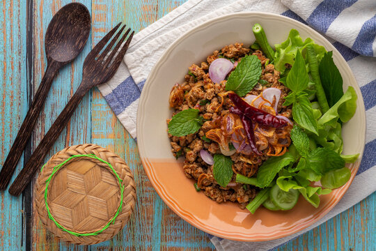 Spicy minced duck salad with vegetables and herbs or laab ped served on a vintage plate on a blue table. Laab is a popular Thai healthy menu from Isan, the northeast of Thailand. Tabletop photography.