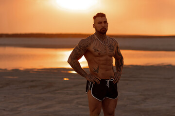 Handsome young muscular italian man posing shirtless on the beach, sunset summer time