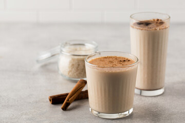 Glasses with a cold drink based on Horchata rice, cinnamon sticks and a jar of rice on a light background.