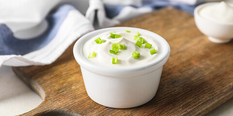 Bowl of tasty sour cream on wooden board, closeup
