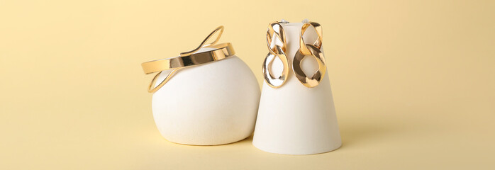 Stylish golden bracelet and earrings on beige background