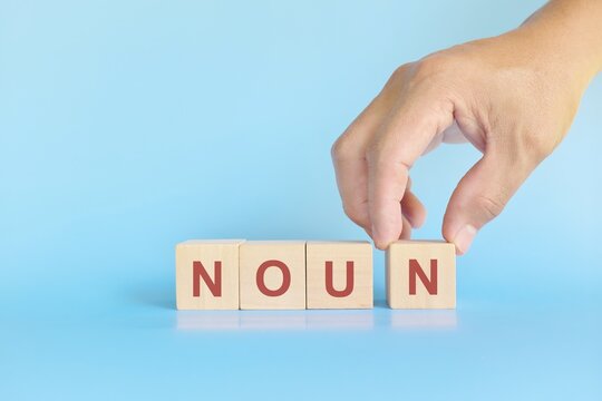 Noun concept in English grammar education. Wooden block crossword puzzle flat lay in blue background.