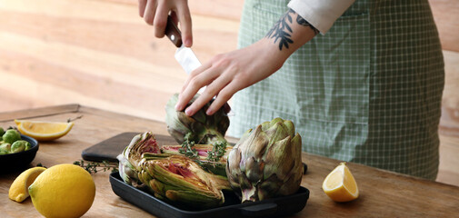 Woman preparing tasty raw artichokes in kitchen, closeup