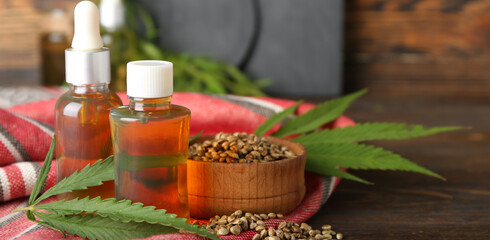 Bottles of hemp oil and bowl with seeds on wooden background
