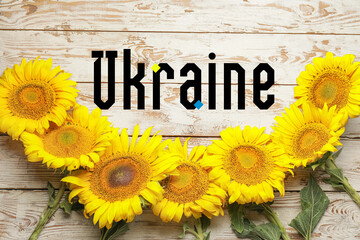 Fresh sunflowers and word UKRAINE on white wooden background