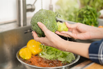 Close up asian young woman washing broccoli, tomato, carrot fresh vegetables, paprika with splash water in basin of water on sink in kitchen, preparing fresh salad, cooking meal. Healthy food people.