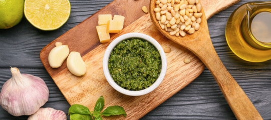 Bowl of fresh pesto sauce and ingredients on dark wooden background