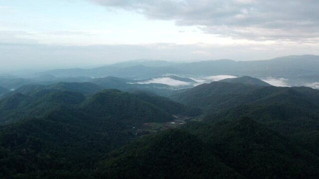 Drone shot flying over beautiful mountain ridge and clouds in rural jungle bush forest .Tree tops against sunny sky.