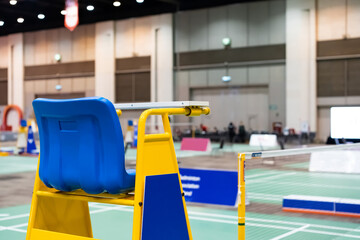 Blue chair of badminton referee with yellow colors near badminton net with blurred background in sport indoor stadium.