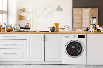 Modern washing machine with white counters in interior of light kitchen