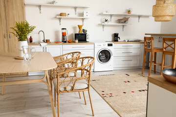 Interior of light kitchen with washing machine, counters and dining table