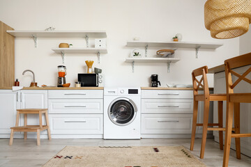 Interior of light kitchen with washing machine, counters and shelves