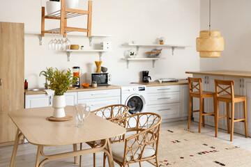 Interior of light kitchen with washing machine, counters and dining table