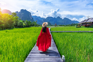 Asian woman standing on a wooden walkway with green rice fields in Vang Vieng, Laos.