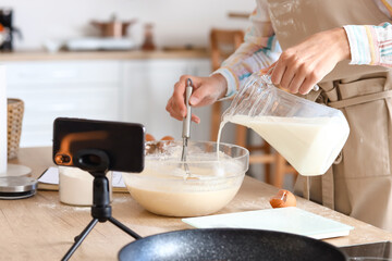 Fototapeta premium Young woman making dough for pancakes while following video tutorial in kitchen, closeup