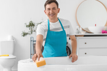 Young man cleaning bathtub with sponge in room