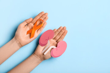 Woman with orange awareness ribbon and paper kidneys on blue background