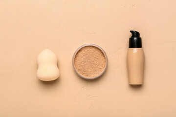 Bottle of makeup foundation, powder and sponge on color background