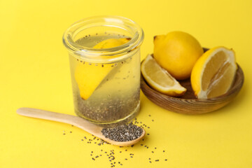 Glass of drink with chia seeds and bowl with lemons on yellow background