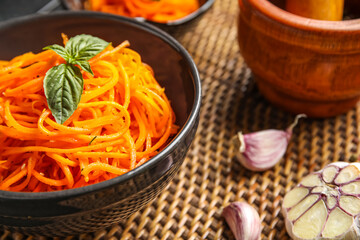 Bowl with spicy carrot salad on wicker mat, closeup
