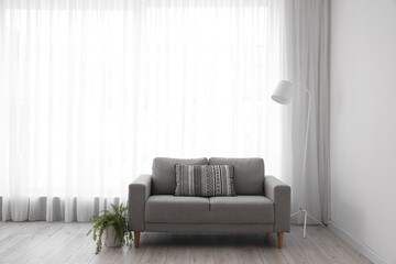 Interior of light living room with grey sofa, standard lamp and houseplant