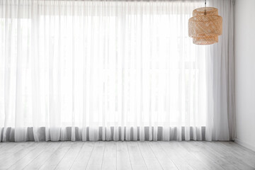 Stylish lamp hanging near light curtain in room