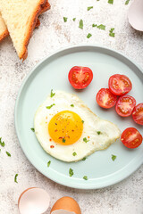 Plate with tasty fried egg and cut tomatoes on light background