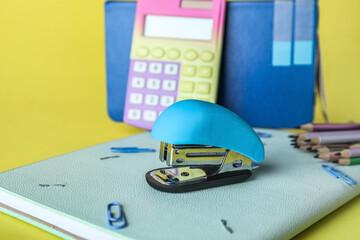 Stapler with stationery supplies on yellow background, closeup