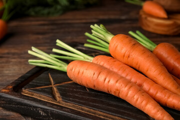 Board with fresh carrots on wooden background, closeup