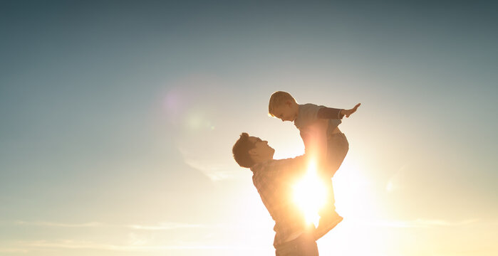 Happy Father Playing With His Son Holding Him Up In The Air. Father Son Relationship Concept.	