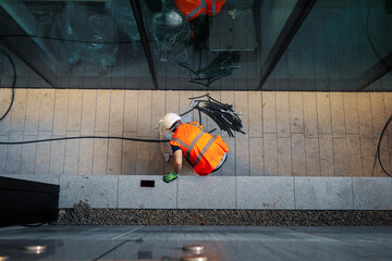Top down view on a construction site worker in orange high visibility vest and white hard safety...